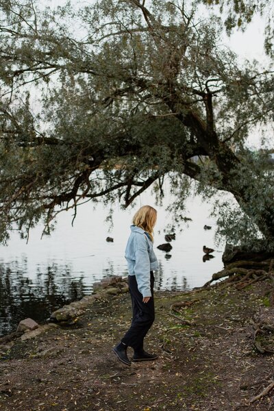 mielen paremminvoinnin ja kehomieliyhteyden valmentaja  kävelee rannalla puiden keskellä