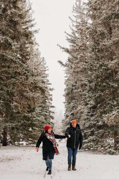 Couple holding hands walking through snowy trees at Assiniboine Park 