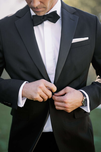 Elegant groom fixing his black tuxedo