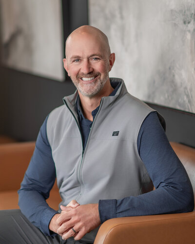A man sits on a couch and smiles as he gets his Iowa photography headshot.