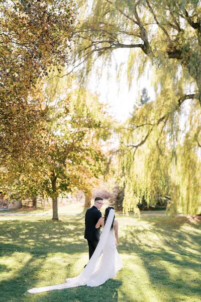 Bride and groom walking through golden trees with long veil flowing behind, photographed at Ontario venue by Toronto-based photographer