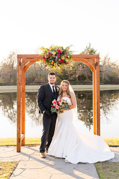 Bride and Groom smiling at their ceremony alter during sunset with a lake behind them at Peach Creek Ranch