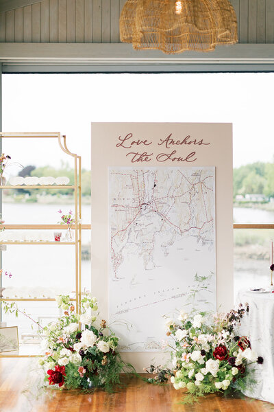 Seating chart installation with nautical map and gold shelf with calligraphy escort cards for Mystic, Connecticut wedding.