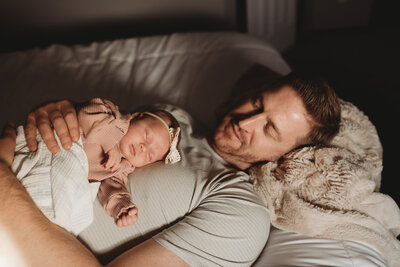 During a in-home newborn session, a dad snuggles with his newborn baby girl.
