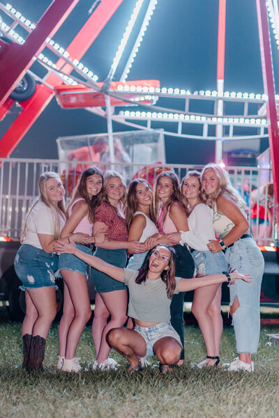 Rachel Hahn, owner of Rachel B Photography, poses with her Senior Rep Team in front of a carnival ride.