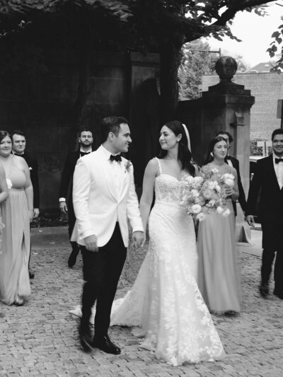 Bride and groom walk with their wedding party as they look at each other.