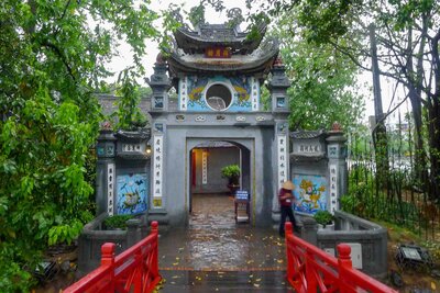The entrance gate to Ngoc Son Temple in Hanoi, framed by lush trees and a red footbridge on a misty day ©Stephanie Dosch | theViatrix Private Luxury Vietnam Travel