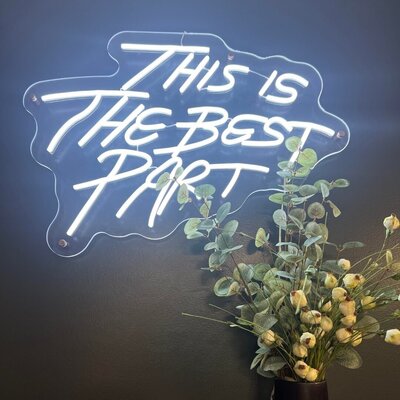 A neon sign reading "This is the best part" mounted on a wall, with a decorative plant beneath it, showcasing the welcoming and positive ambiance of 212 Salon, Spa, & Barbershop.