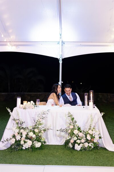 A newlywed couple laughing as they sit at a table together 