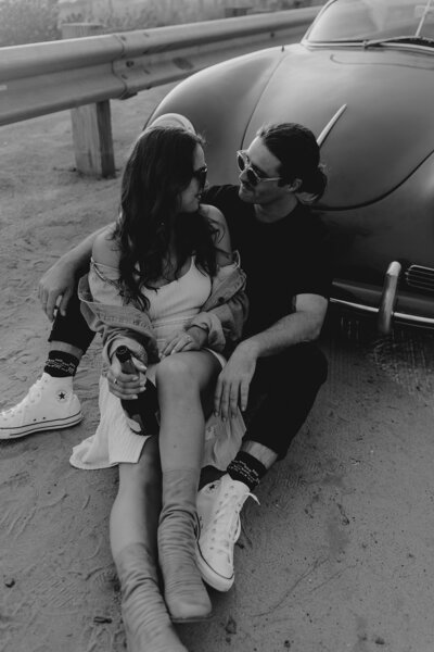 couple embrace next to classic car for engagement photos in san diego