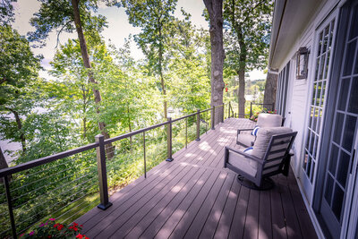 Deck overlooking dense trees on a sunny summer day, with TimberTech Impressions aluminum railing with horizontal cable infill. 