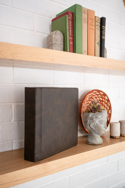 Handcrafted wedding album displayed on a minimalist wooden shelf with vintage books and artistic decor.