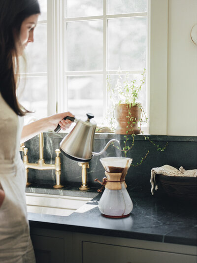 a designer pours pour over coffee at Fernhaus, Northern Michigan, during her brand photoshoot on film