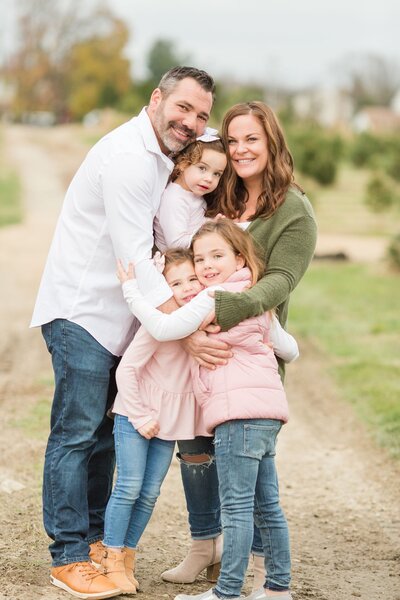 Family with 3 young kids hugging and smiling at the camera