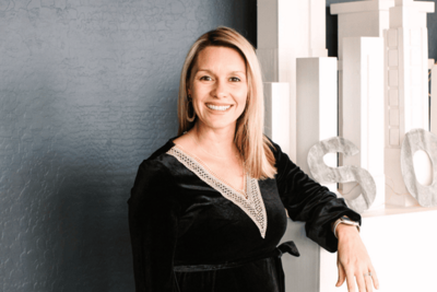 Megan Schmidt, CEO and owner of SoHo63, a Chandler wedding and event venue, smiles while posing indoors against a modern backdrop featuring neutral architectural decor. Her confident and welcoming presence reflects the leadership behind this popular Arizona event space.
