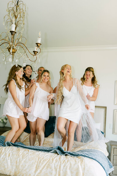 Bride and bridesmaids in white robes celebrating together on the wedding morning in Oklahoma, captured in a refined and joyful style