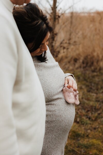 Mutter hält kleine Babyschuhe über ihren Babybauch