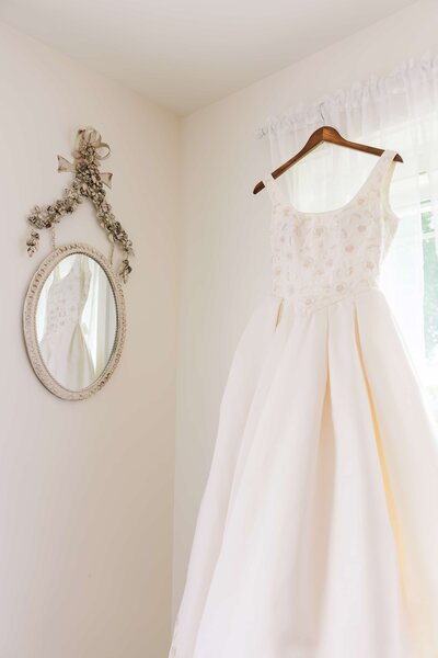 White wedding dress with embroidered flowers hanging up in the window of a wedding bridal suite