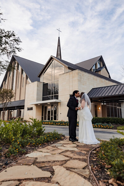 newly married couple sharing a romantic moment in front of Tallowood Chapel in Houston, Texas, with the beautiful chapel architecture as a backdrop on their wedding day.