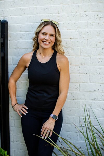 woman with blonde hair in black activewear on white brick wall outside