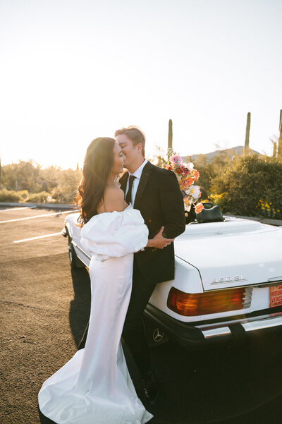 Bride and groom embracing as they lean on vintage getaway car
