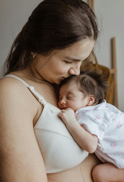 New Jersey Woman holding and kissing her newborn baby while wearing a pumping bra