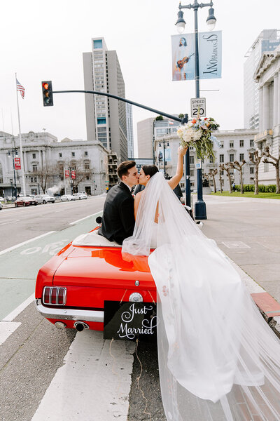 newlyweds pose in classic car in front of city hall