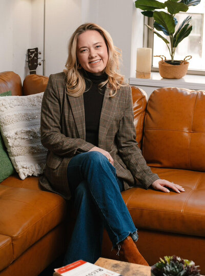 Olivia Verhulst, psychotherapist sitting on a leather couch smiling at the camera.