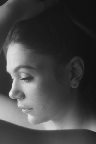 Portrait mélancolique d'une jeune femme tournée vers une fenêtre et regardant vers le bas, lors de sa séance photo portrait à Lyon