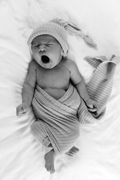 A yawning newborn swaddled in a soft blanket. Photographed by Sophie Louise for Nostalgia.