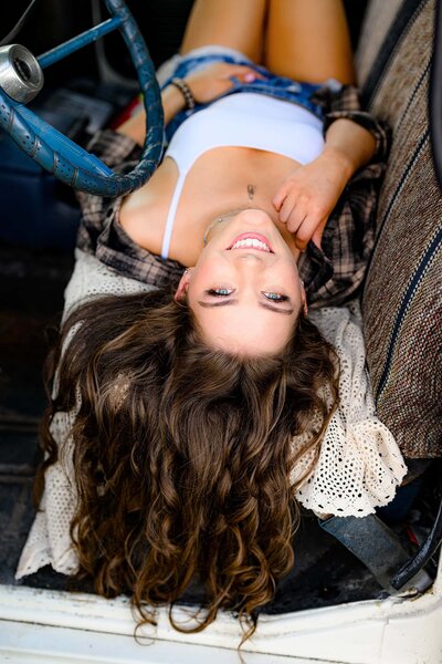 senior girl wears white tank and flannel with jean shorts as she lays in a truck seat
