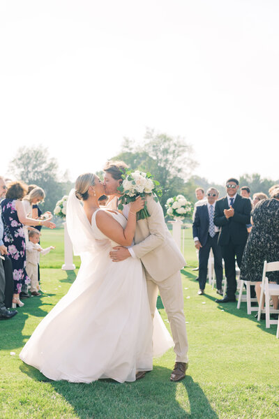 Bluestone Estate couple sharing a kiss with champagne in hand, celebrating their wedding day on a scenic dock.