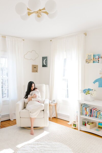 A mother snuggles her newborn baby in a sunlit nursery during her NJ newborn photos.