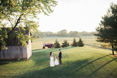 Bride, groom, and flower girl walk across a field