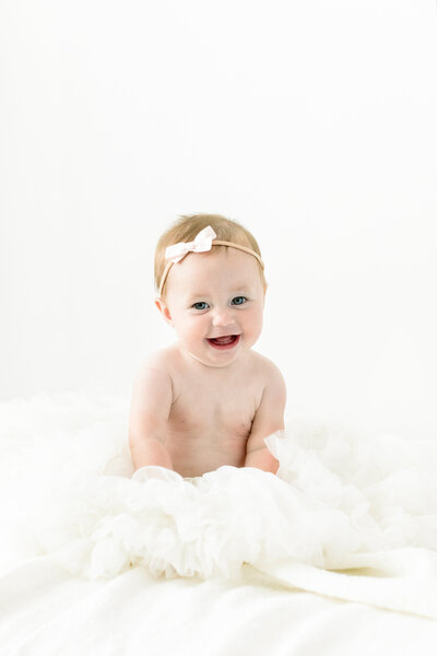 baby in large tutu and bow sitting on blanket