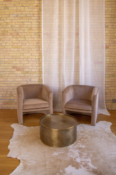 Two mauve velvet chairs and a round brass coffee table.