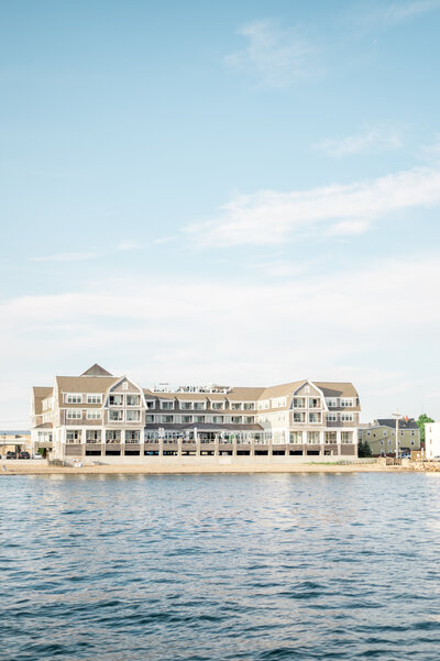 A pulled-back view of the Beauport Hotel captured from the water, showcasing its stunning beachfront location and timeless New England coastal architecture.