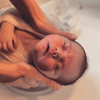 Deux mains qui tiennent la tête d'un bébé détendu dans son bain