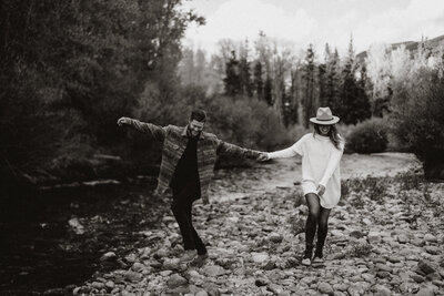 Engaged couple walking along a rocky riverside trail, showcasing adventurous love in Breckenridge, Colorado.