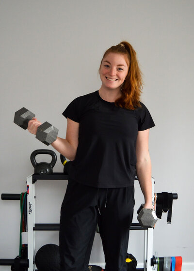 Virtual Trainer standing holding dumbbells and smiling