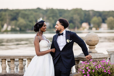 Bride and groom pose for a regal and affectionate photo by the water's edge, framed by lush greenery and florals near Grand View Mendon MA