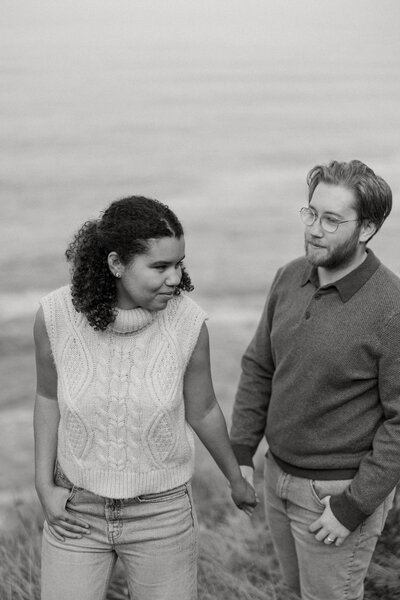 A couple holding hands and walking along a grassy cliff 
