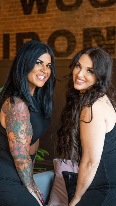 Jess and Santina smiling at the camera wearing black dresses in the hair salon.