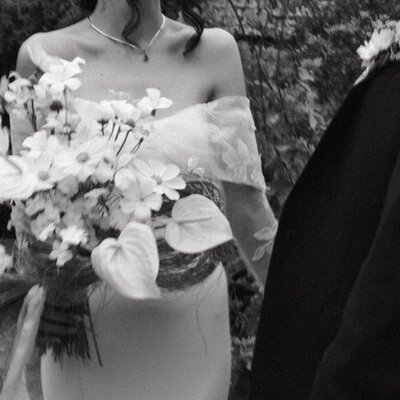Bride in a v neck wedding dress wearing a top knot standing with floral bouquet