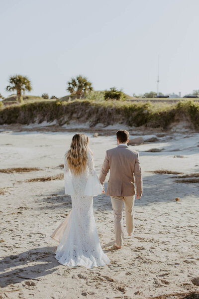 Bride and groom in tan tux holding hands and walking during sunrise elopement at the beach