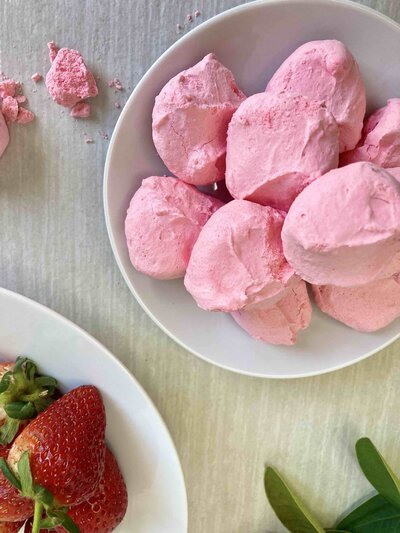 Pink meringues in white bowl with strawberries.