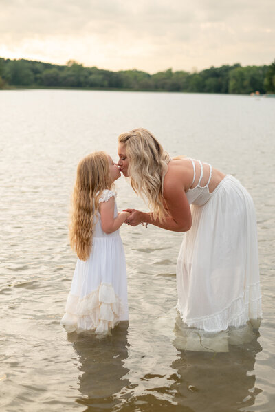 Mommy and daughter sharing a kiss while standing in water at the beach.