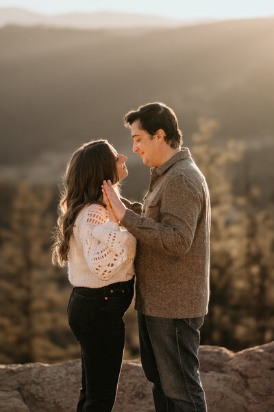 Man and woman stand on mountain overlook during engagement photos,