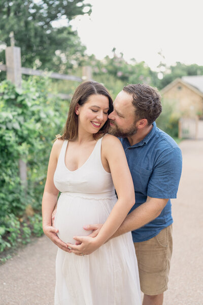 Pregnant woman in white dress and her husband standing in a botanical garden.