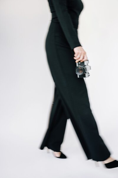 Naomi, a destination wedding photographer, holding a camera and walking out of frame.